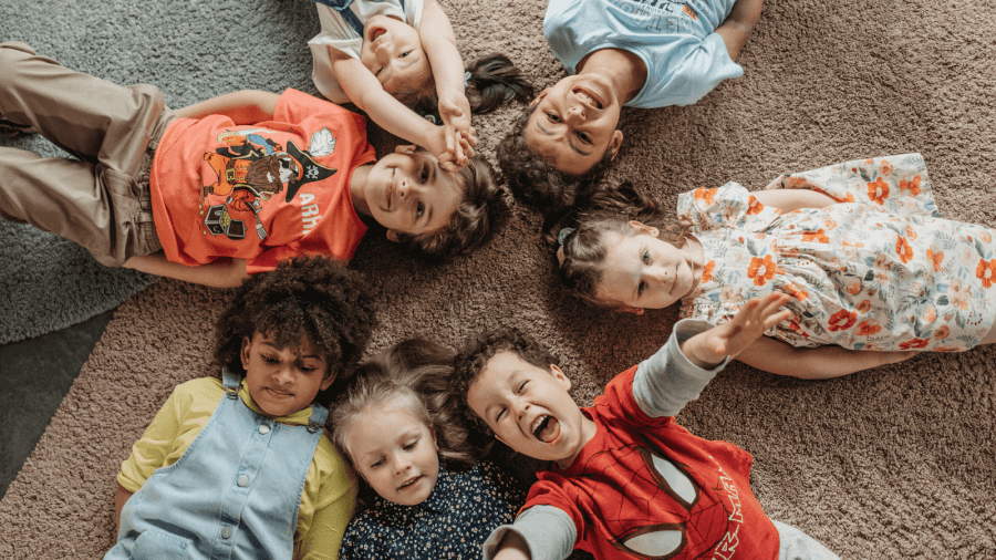 kids_optimized seven smiling children lying down with heads touching in a circle formation