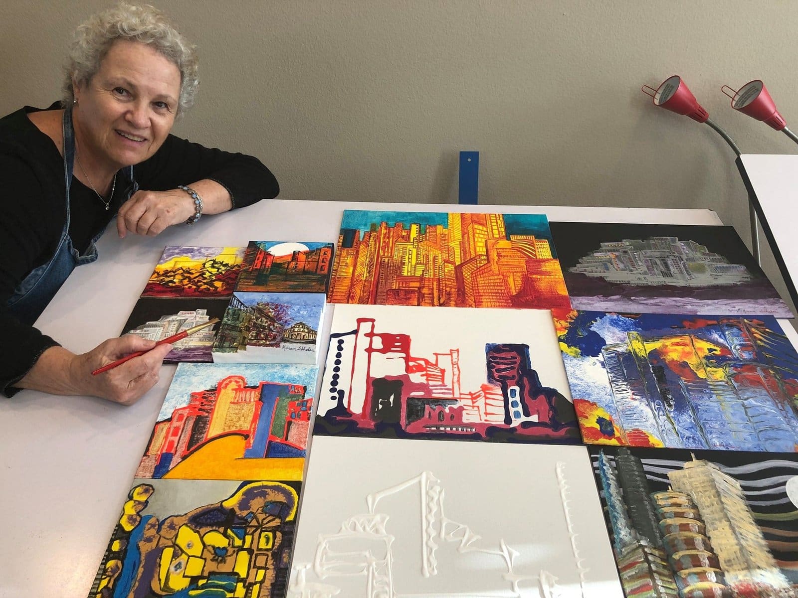 Miriam Libhaber Miriam Libhaber posing next to her artwork spread on the table.