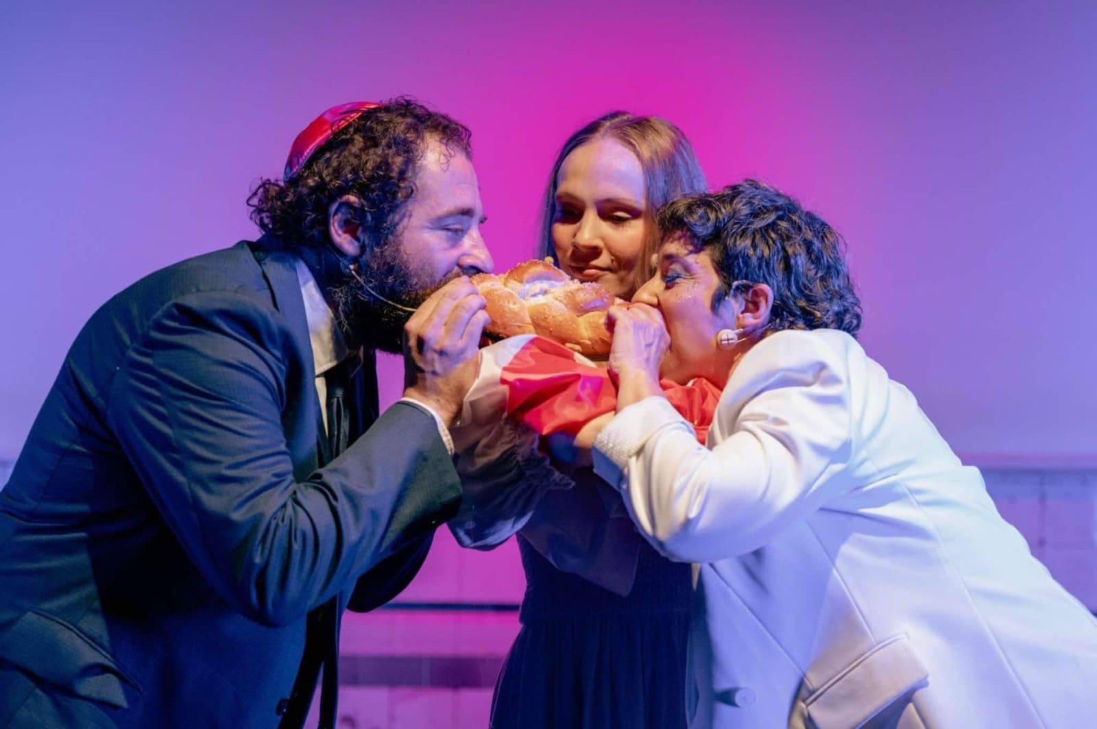 Promotional image for the play Poland is not yet lost Michael Rubenfeld Dorota Abbe and another actor in costumes, all biting into a loaf of challah.